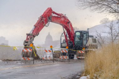 Kışın karlı bir dağ yolunda kırmızı ekskavatör ve barikatlar