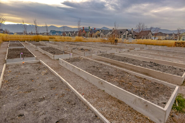Raised garden beds with homes and mountain against cloudy sky in the background