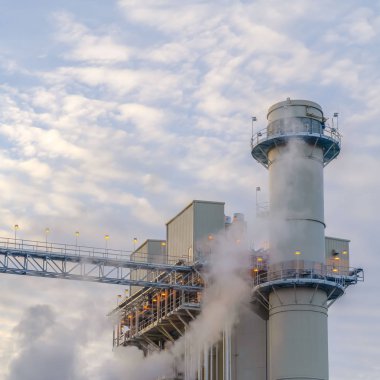 Kulenin arkasında kabarık bulutlar ve bir Elektrik Santrali binaları ile Kare Mavi gökyüzü