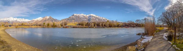 Panorama panorâmico de um lago contra a montanha coberta de neve e o céu azul no inverno — Fotografia de Stock