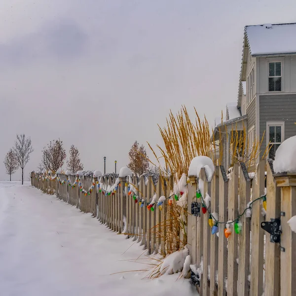 Camino cuadrado claro en el suelo cubierto de nieve a lo largo de una valla con luces de colores en invierno — Foto de Stock