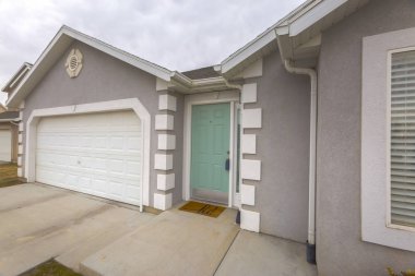 Bulutlu bir gökyüzüne karşı yeşil ön kapı ve beyaz garaj kapısı ile ev cephesi