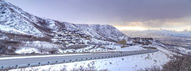 Kışın bulutlu gökyüzüne karşı karla kaplı bir dağ boyunca kıvrılan yol