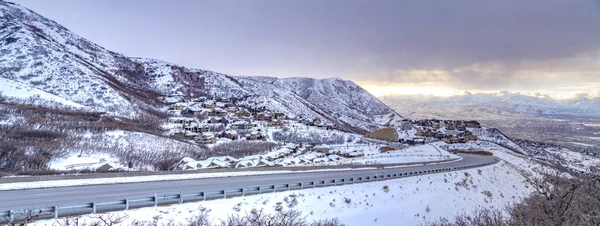 Kışın bulutlu gökyüzüne karşı karla kaplı bir dağ boyunca kıvrılan yol