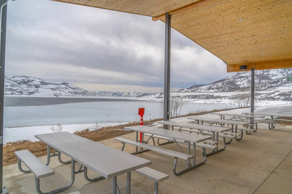 Área de comer dentro de um pavilhão com vista para um lago em meio à paisagem nevada — Fotografia de Stock