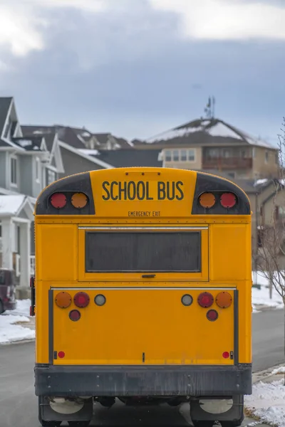 Задняя часть жёлтого школьного автобуса против снежных домов и облачного неба зимой — стоковое фото
