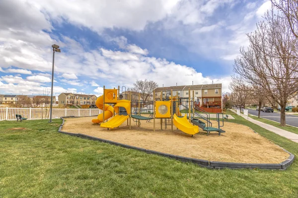 Colorful slides at a playground with homes and cloudy sky in the background