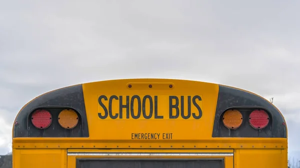 Clear Panorama Rear of a yellow school bus with signal lights and emergency exit window