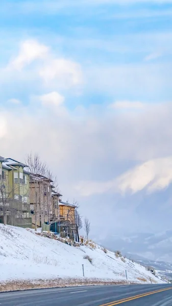 Vue panoramique verticale claire de maisons colorées sur une pente enneigée le long d'une route goudronnée en hiver — Photo