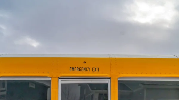 Panorama CLose up of the exterior of a yellow school bus against cloudy sky