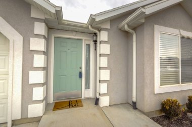 Bulutlu gökyüzüne karşı görüntülenen ev cephesinde yan ışıklı yeşil ön kapı