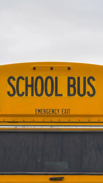 Pionowe zbliżenie tylnej strony żółtego autobusu szkolnego z domów i pochmurne niebo — Zdjęcie stockowe