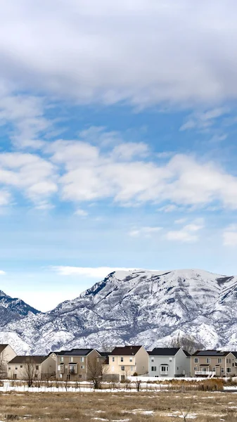 Вертикальне Прекрасне блакитне небо з пухнастими хмарами над будинками і горою взимку — стокове фото