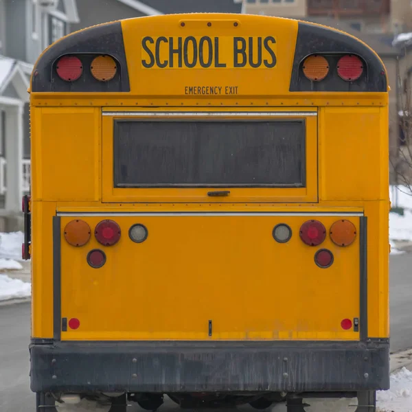 Чистая площадь, желтый школьный автобус на фоне заснеженных домов и облачного неба зимой — стоковое фото