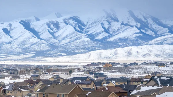 Maisons panoramiques claires avec une montagne enneigée et un ciel nuageux en arrière-plan vu en hiver — Photo