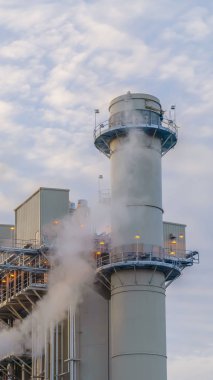 Kulenin arkasında kabarık bulutlar ve bir Elektrik Santrali binaları ile Dikey Mavi gökyüzü