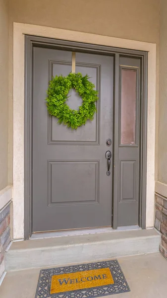 Verticale grijze voordeur van een huis met een eenvoudige groene krans en zijlicht — Stockfoto