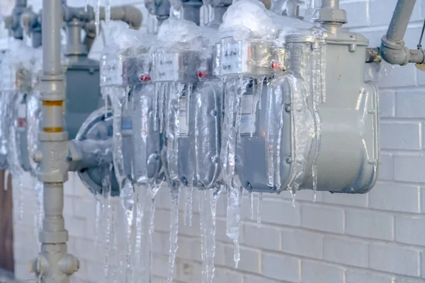 Water meters and gray pipes covered with against a white brick wall