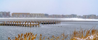 Kışın gölün ötesinde karla kaplı bir arazide gökyüzüne karşı binalar