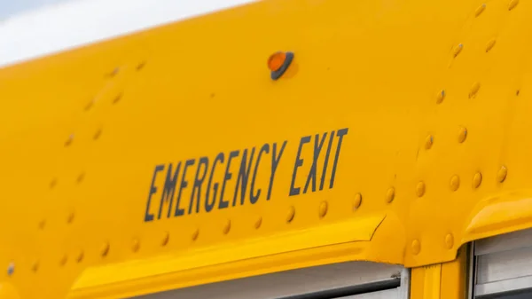 Panorama Close up of the exterior of a yellow school bus with an Emergency Exit sign