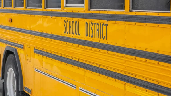 Панорама Закрытие автобуса жёлтой школы на снежной дороге против домов и облачного неба — стоковое фото