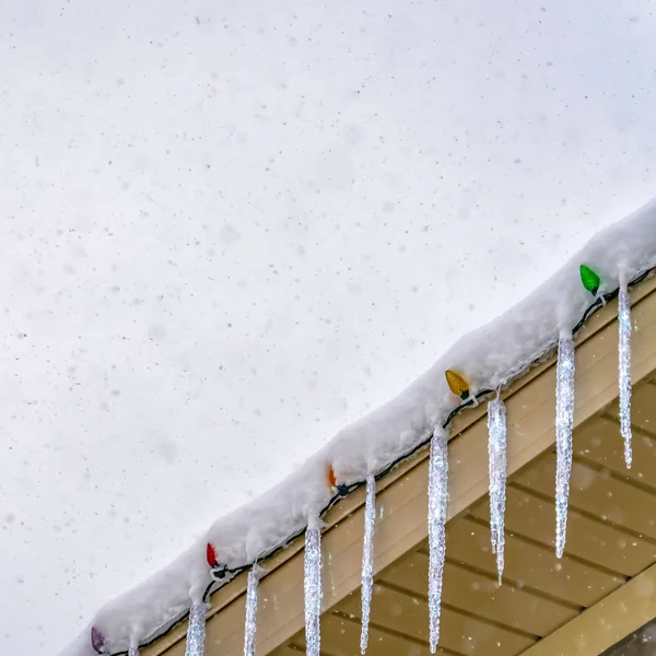 Cubierta de nieve cuadrada techo con carámbanos y luces de colores contra un cielo nublado — Foto de Stock