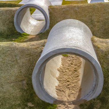 Güneşli bir oyun alanında beton silindir borulardan yapılmış kare çerçeve Crawl tüneller
