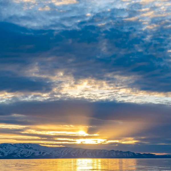 Marco cuadrado Sol dorado que brilla a través del cielo nublado y se refleja en el lago brillante debajo —  Fotos de Stock