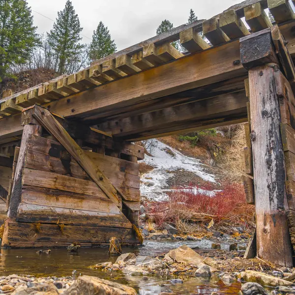 Ponte de madeira rústica quadrada atravessando um riacho rochoso com águas rasas claras — Fotografia de Stock