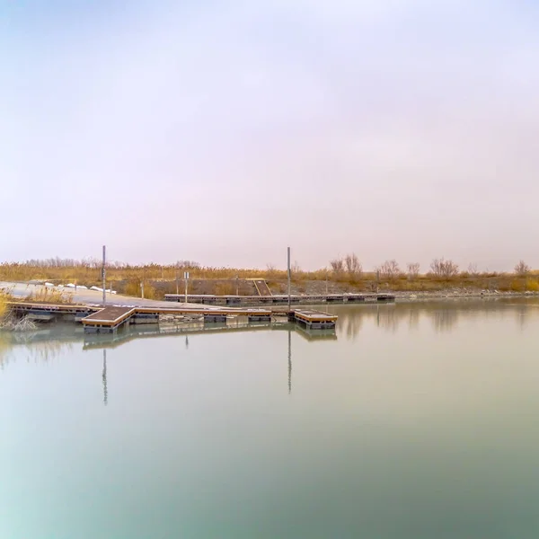 Lago reluzente quadrado com reflexos de gramíneas exuberantes e céu nublado em sua superfície — Fotografia de Stock