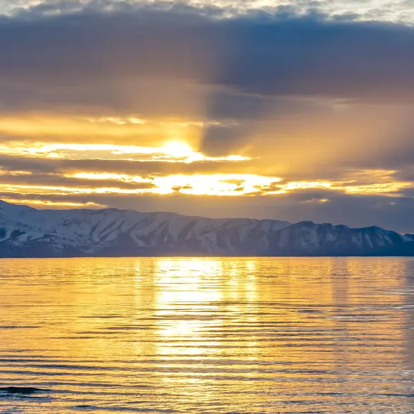 Sol dorado cuadrado que brilla a través del cielo nublado y se refleja en el lago brillante debajo —  Fotos de Stock