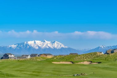 Mavi gökyüzü altında göl ve karla kaplı dağ manzaralı yemyeşil çimenli arazi