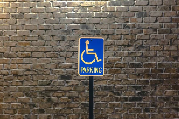 Handicap sinal de estacionamento contra uma parede de tijolo de pedra iluminado por — Fotografia de Stock
