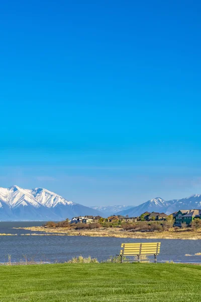 Pohled na lavičku na poli s výhledem na jezero s domy n — Stock fotografie