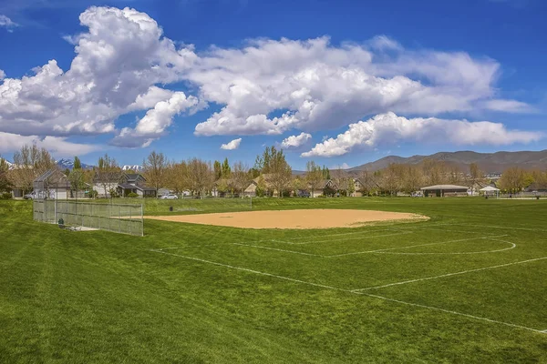 Terrain de baseball ou de softball avec bâtiments et arbres au-delà du terrain herbeux — Photo