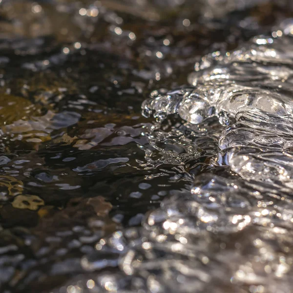 Cuadrado Primer plano de un arroyo con agua congelada translúcida sobre rocas oscuras —  Fotos de Stock