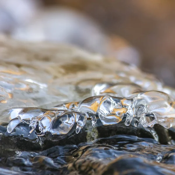 Square Primer plano de agua helada lisa y translúcida que cubre rocas oscuras —  Fotos de Stock
