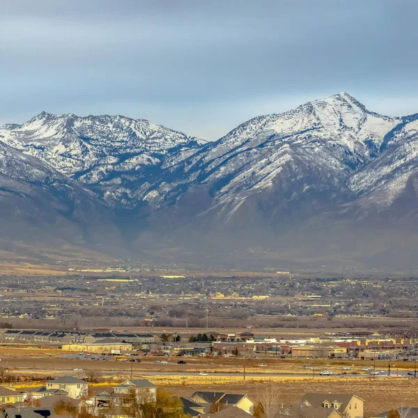 Panorama cuadrado de una montaña cubierta de nieve que se eleva sobre las casas en el vasto valle — Foto de Stock