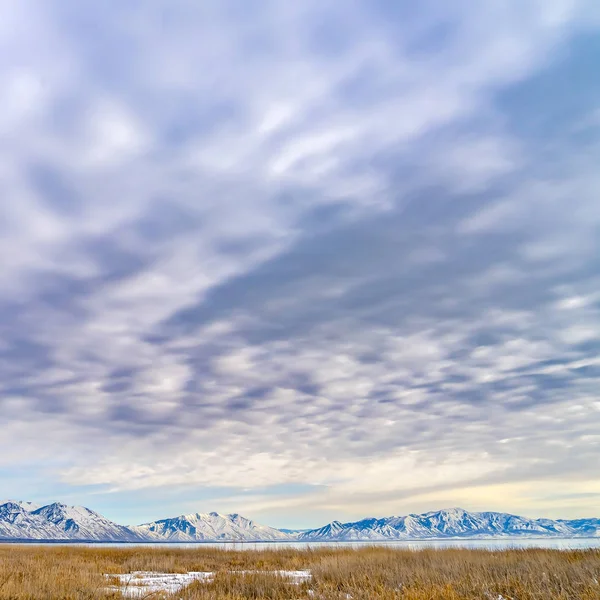 Panorama carré cadre d'une montagne givrée et d'un lac sous un ciel magnifique rempli de nuages — Photo