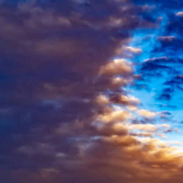 Vierkante gedeconcentreerde weergave van een uitgestrekte blauwe hemel gevuld met gezwollen donkere wolken bij zonsondergang — Stockfoto