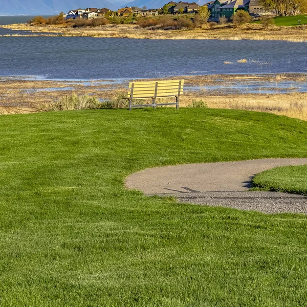 Quadratischer Weg und Bank auf einem Feld mit Blick auf den See unter blauem Himmel an einem sonnigen Tag — Stockfoto