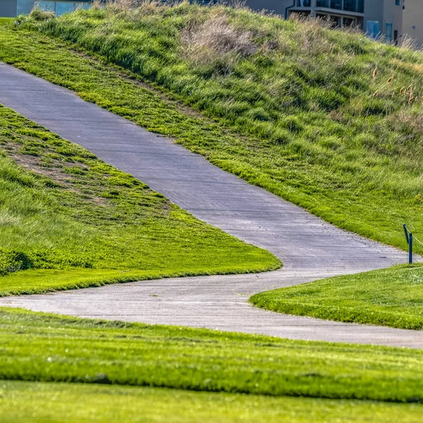 Quadratische gepflasterte Straße, die auf einem Hügel mit sattgrünen Gräsern verläuft, an einem sonnigen Tag gesehen — Stockfoto