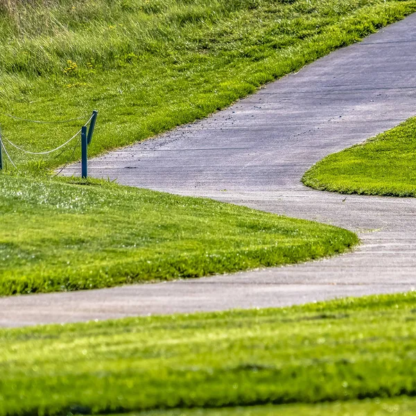 Rahmen quadratische gepflasterte Straße, die auf einem Hügel mit sattgrünen Gräsern an einem sonnigen Tag gesehen verläuft — Stockfoto