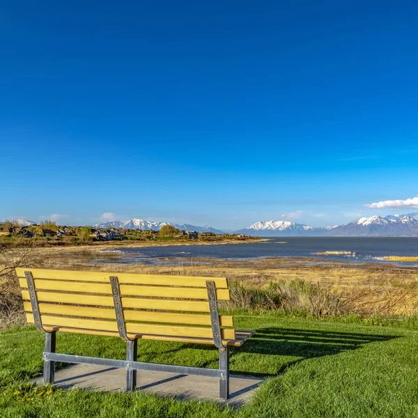 Čtvercový lavička na travnaté polní hřiště s výhledem na jezero a zasněženou horu proti modrému nebi — Stock fotografie