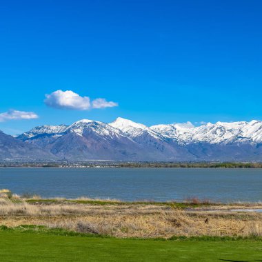 Çerçeve Kare Kare Ön planda kahverengi otlar ve güneşli alan ile bir gölün panoramik görünümü