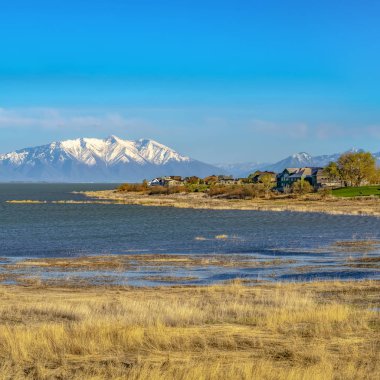 Güneşli bir günde çimenli kıyı ve pırıl pırıl su ile bir gölün önünde Çerçeve Kare Evler