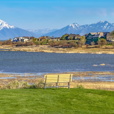 Pırıl pırıl bir göle bakan çimenli bir alanda Kare Kıvrımlı yol ve boş bank