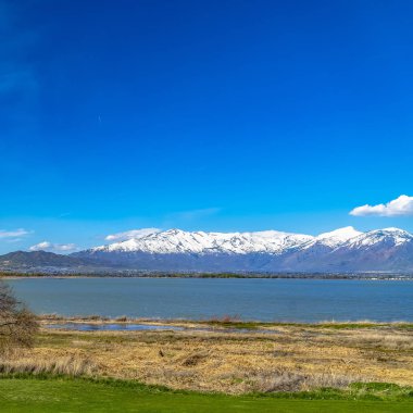Canlı mavi gökyüzü altında karlı zirve ile sakin bir göl ve dağ Çerçeve Kare Panorama