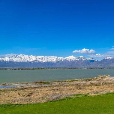 Güneşli bir günde izlenen çimenli kıyı ile bir gölün önünde Kare Gür yeşil alan