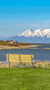 Yemyeşil arazide, çimenli kıyısının yakınında inşa edilmiş evlerin bulunduğu bir göle bakan Panorama Bench